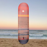 Balade à travers Golden Orange Sunset Skateboard<br><div class="desc">Cette planche à roulettes présente l'image d'une personne qui marche à travers les rayons dorés rose et orange du coucher du soleil. Les rayons colorés créent une orbe qui silhouette le marcheur.</div>