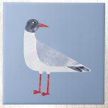 Carreau Oiseau marin bleu ciel<br><div class="desc">Une mouette noire amusante et coquine qui se tient près de l'océan. Parfait pour les amateurs de la côte. Art original de Nic Squirrell.</div>