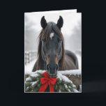 Carte Cheval de Noël<br><div class="desc">Un cheval se tient derrière une clôture en bois ornée d'une couronne festive et d'un arc rouge,  entourée d'un paysage hivernal enneigé. Le texte intérieur peut être modifié.</div>