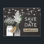 Carte Postale Faire-part Pays Rustic Chalkboard Wood Enregistrer la date<br><div class="desc">LES LUMIÈRES DE CHAÎNE MASON JAR ENREGISTRENT LE MODÈLE DATE | Un arrière - plan de tableau noir rustique, des lampes à corde, un pot de maçon et une bouteille avec une étiquette cadeau nouée autour avec les initiales des couples, des fleurs blanches douces, un morceau de bois de pays...</div>
