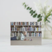 Carte Postale Lecture par une femme âgée par bibliothèque (Debout devant)