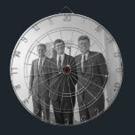 Cible De Fléchettes Le président John Kennedy et les frères American C<br><div class="desc">Le soleil frappa les trois frères Kennedy alors qu'ils se tenaient sous le portique blanc familier de la Maison Blanche. Le président John F. Kennedy, l'aîné, s'appuyait sur un pilier, un sourire irréfléchi jouant sur ses lèvres. Ses frères plus jeunes, Robert et Ted, se tenaient à ses côtés, et leurs...</div>
