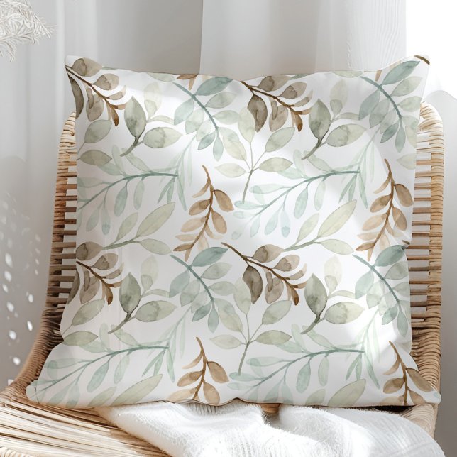 Coussin Feuilles aquarelles vert sauge et marron (Sage Green and brown watercolor leaves on a white throw pillow in a rattan armchair.)