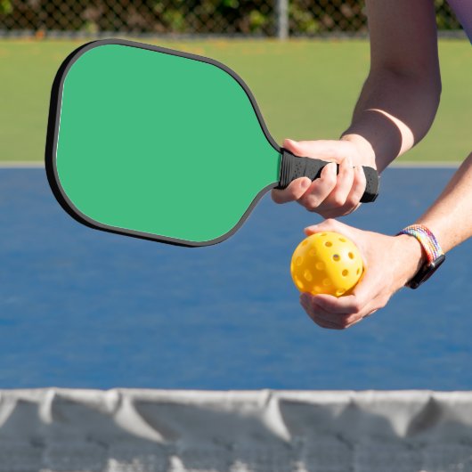 Een groene achtergrond met een witte rand pickleball paddle (Insitu)
