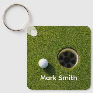 Golfbal naast hole op groene gras golfbaan sleutelhanger
