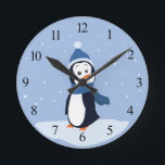 Horloge Ronde Penguin (with numbers)<br><div class="desc">A penguin wearing a blue hat and scarf stands in the snow and watches the snowflakes fall. This design is available on multiple products including shirts,  mugs,  pillows,  and more! It can be customized or personalized by adding your own text or images!</div>
