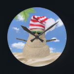 Horloge Ronde Tropical Christmas Sand Snowman<br><div class="desc">Sable de Noël tropical bonhomme de neige avec casquette rayé rouge et blanc et lunettes de soleil vert sur le sable.</div>