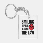 In het openbaar glimlachen is tegen de wet sleutelhanger (Voorkant Links)