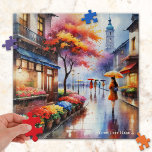 Jour de pluie coloré dans le Puzzle d'aquarelle de<br><div class="desc">Puzzle représentant une aquarelle d'une fille avec un parapluie qui passe devant un fleuriste par jour de pluie en ville.</div>