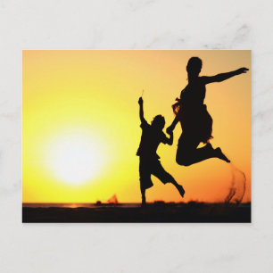 Moeder en zoon silhouettes die op het strand sprin briefkaart