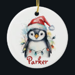 Pingouin Ornement de Noël personnalisé<br><div class="desc">Célébrez la saison avec cet adorable ornement de Noël personnalisé de pingouins ! Doté d’un pingouin à l’aquarelle portant un chapeau de Père Noël et enveloppé de lumières de fête colorées, ce garde-robe en céramique inclut le nom de votre enfant dans un script rouge festif. Cet ornement, qui s’ajoute parfaitement...</div>