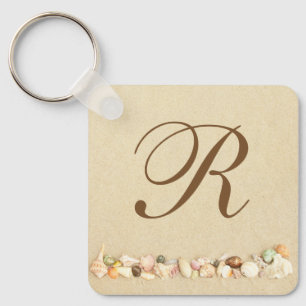 Rij zeeshells op strand zand met monogram sleutelhanger