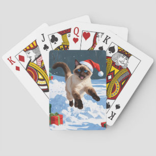 Siamees kat loopt in de sneeuw met kerstmuts pokerkaarten