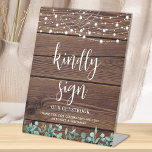 Signe De Table Mariage Invité Rustique Bois vert Lumières à corde<br><div class="desc">Invités Invitations à signer votre livre d'hôtes mariage avec cette maison d'hôtes personnalisée moderne mais rustique eucalyptus verdure et lampes à cordes mariage panneau de réservation d'invités. Cette affiche de livres d'hôtes mariage de verdure présente d'élégants feuilles botaniques, des lampes à cordes sur le bois rustique de la grange de...</div>