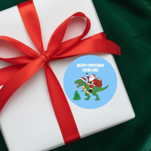 Sticker Rond Père Noël drôle à cheval sur un T-Rex Noël