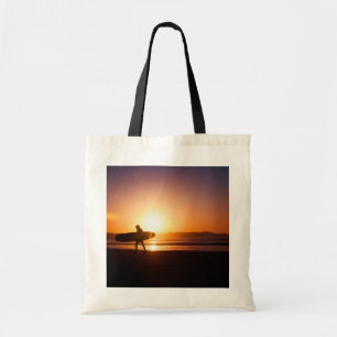 Surfer met surfplank op het strand bij zonsonderga tote bag