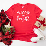 T-shirt Joyeux et brillant Noël des femmes rouges modernes<br><div class="desc">Un tee-shirt graphique festif pour les femmes avec une typographie en minuscules moderne avec "Joyeux et brillant". Le texte blanc et le style de t-shirt rouge peuvent tous deux être modifiés.</div>