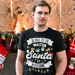 T-shirt Soyez gentil avec le serveur que Père Noël regarde<br><div class="desc">Rappelez à vos clients de rester sur la belle liste cette année avec ce joli t-shirt de Noël amusant et joli avec le libellé "Soyez gentil avec le serveur, Père Noël regarde" en polices modernes noires, décoré de lumières de Noël rouges, vertes et jaunes, flocons de neige noirs, chapeau de...</div>