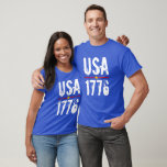 T-shirt USA 1776<br><div class="desc">USA et 1776 dans une police unique est imprimé en blanc sur ce T-shirt unisex surligné de rayures rouges et bleues et d'une étoile d'or. Choisissez la couleur et la taille de votre T-shirt parmi celles disponibles.</div>
