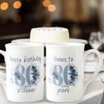 Tasse En Porcelaine 80e anniversaire Cheers à 80 ans Numéro floral<br><div class="desc">80e anniversaire tasse, avec une formulation entièrement modifiable pour personnaliser comme vous le souhaitez, comme "heureux anniversaire [nom]" et/ou "applaudissements à 80 ans". Le design comporte le numéro 80 décoré avec des bourgeons roses, fleurs et feuillage dans les tons bleu côtier et sable. Design féminin et élégant subtil avec des...</div>