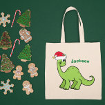 Tote Bag Joli Dinosaure de Noël Personnalisé Vert Enfants N<br><div class="desc">Un dinosaure vert magnifique qui a l'air très mignon dans un chapeau de Noël rouge de vacances avec un petit sourire. Adorable cadeau sac fourre-tout personnalisé pour enfant pour votre petit garçon ou fille.</div>