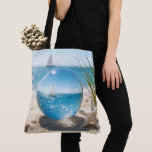 Tote Bag Ocean Reflection in a Lens Ball<br><div class="desc">A sailboat on a sunlit ocean, its reflection captured in a glass lens ball on beach sand next to a starfish</div>