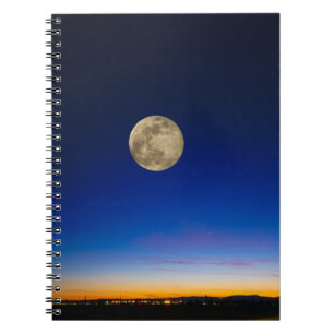 Volle maan stijgt boven zonsondergang notitieboek