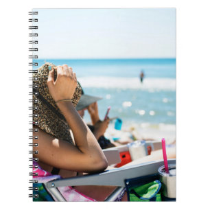 Vrouw die op zonlounger ligt en haar gezicht bedek notitieboek